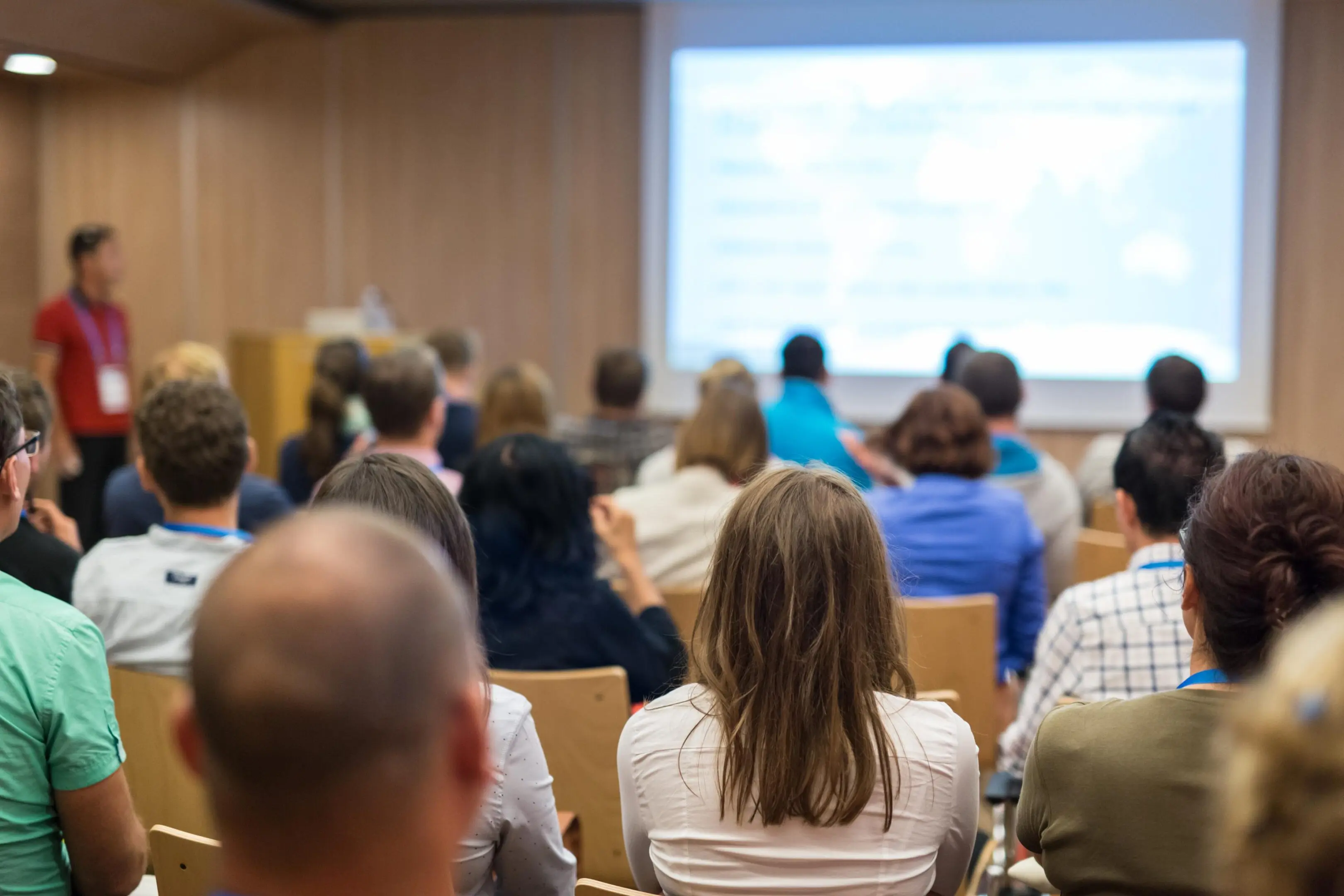 Business and entrepreneurship symposium. Speaker giving a talk at health care workshop meeting. Audience in conference hall. Rear view of unrecognized participant in audience.